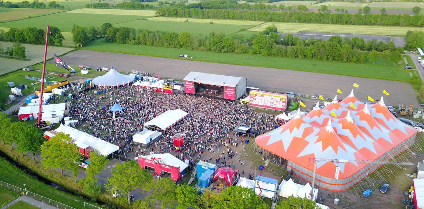 Luchtfoto van een festivalterrein met podium, tenten en publiek
