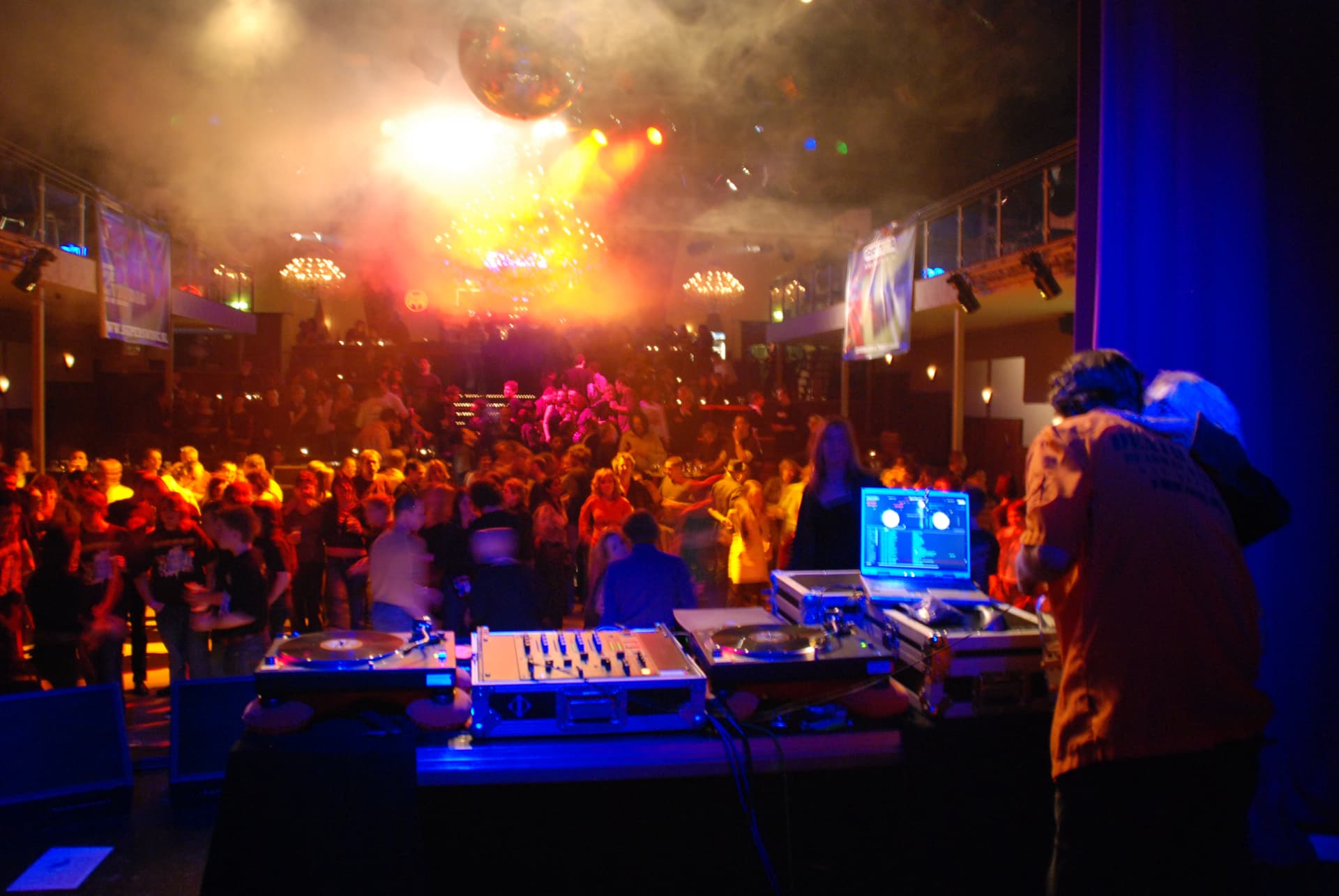 Dansvloer vol publiek met discobal en kleurrijke lichtshow